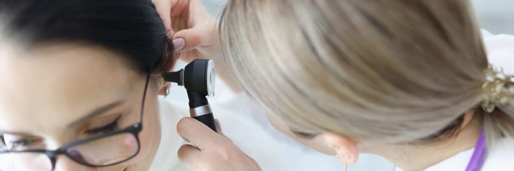 Otorhinolaryngologist doctor examining patients ear with otoscope in clinic. Deafness diagnostics concept